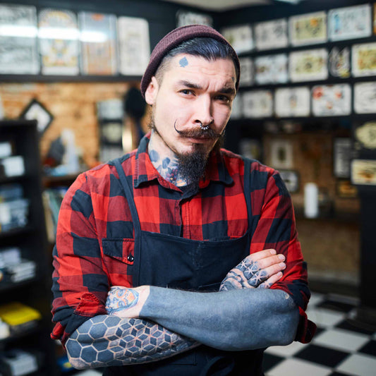 Piercer with tattoos looking skeptical with his arms folded