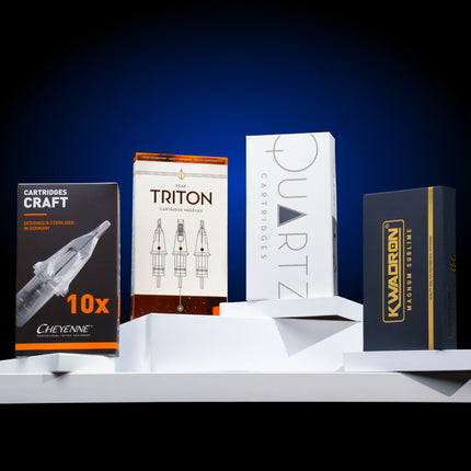 Box of Peak Triton cartridge needles, Cheyenne Craft cartridge needles, Peak Quartz cartridge needles, and Kwadron cartridge needles all on a table