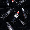 Bottle of Dynamic Triple Black, Maxx Black, Blackour, Zuper Black, and Blak tattoo inks on a black backdrop with broken shards of glass