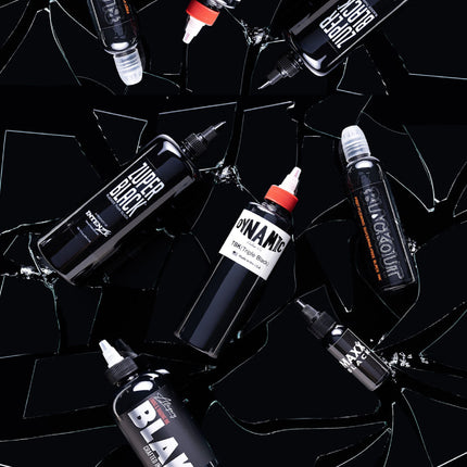 Bottle of Dynamic Triple Black, Maxx Black, Blackour, Zuper Black, and Blak tattoo inks on a black backdrop with broken shards of glass