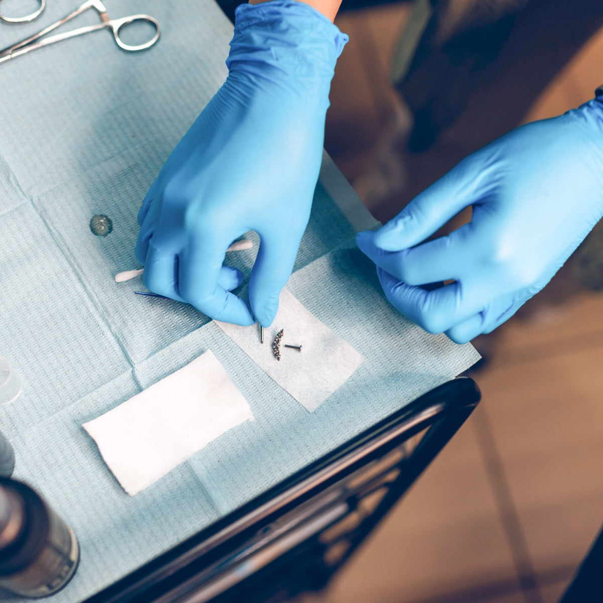 Gloved piercer preparing body jewelry and tools on a covered tray. Best Body Jewelry for Fresh Piercings - Titanium, Implant-Grade, & APP Standards