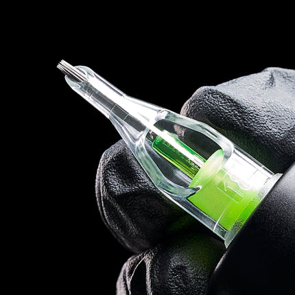 Gloved hand holds a green tattoo cartridge with its needle grouping exposed.