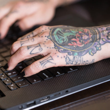 Colorful hand and finger tattoos on a hand typing on a laptop.