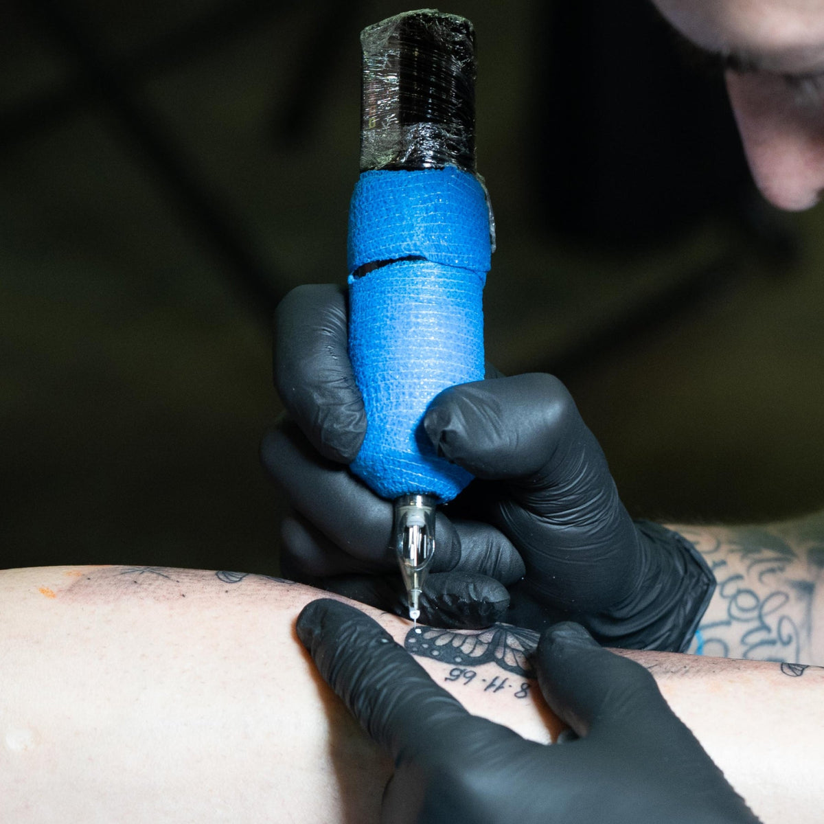 Artist adding white ink details with a battery-powered tattoo machine wrapped in blue grip tape. 10 Tips to Extend Your Tattoo Machine Battery Life