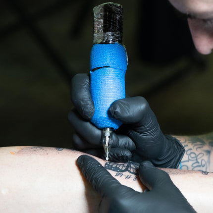Artist adding white ink details with a battery-powered tattoo machine wrapped in blue grip tape.