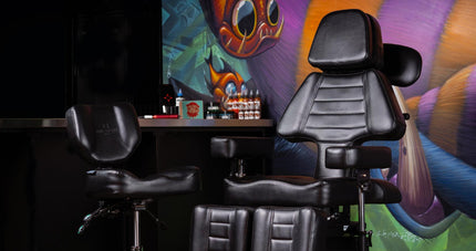 Fellowship tattoo client chair and artist chair in front of a table with a tattoo setup against a mural wall