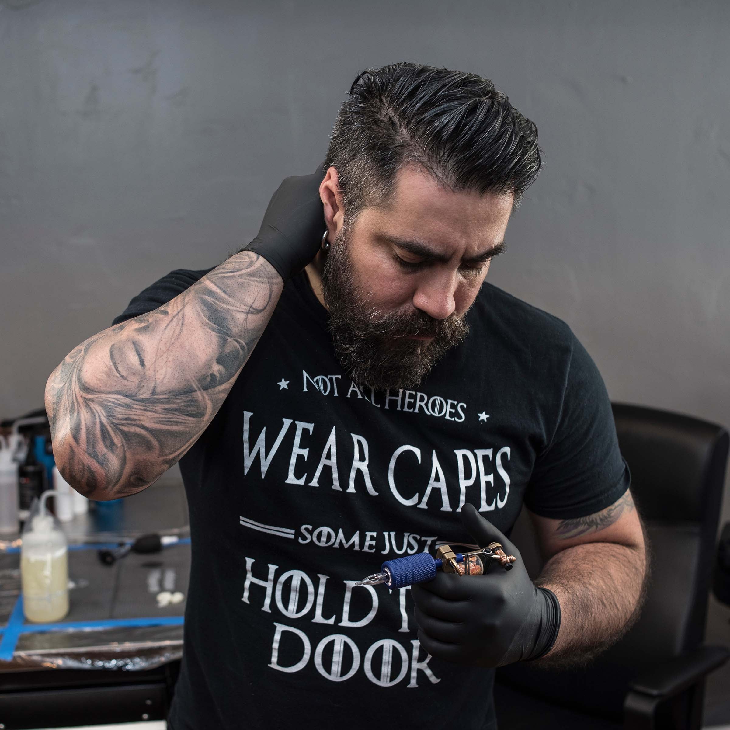 Tattoo artist with beard and latex gloves looking at his tattoo machine Achieving Physical and Mental Health for Tattoo Artists: Our Top 10 Tips
