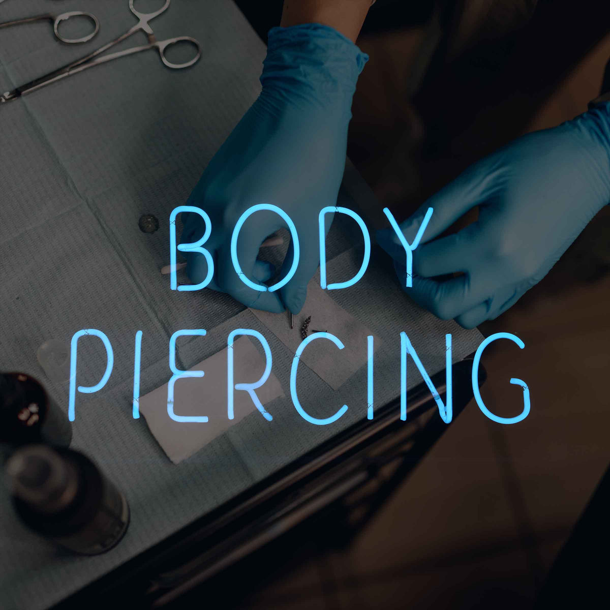 Neon body piercing sign over top an artist using piercing tools