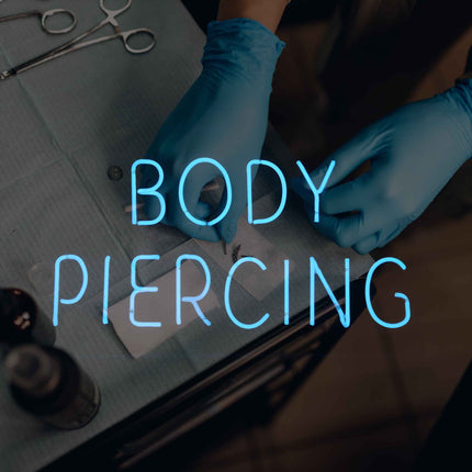 Neon body piercing sign over top an artist using piercing tools