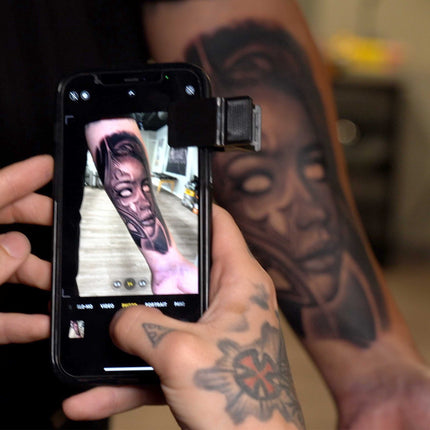 Tattoo artist using his iPhone with a CPL filter to take a picture of an arm tattoo. The tattoo is on a client's inner forearm. It is a black and gray lady head tattoo in a surrealist style..