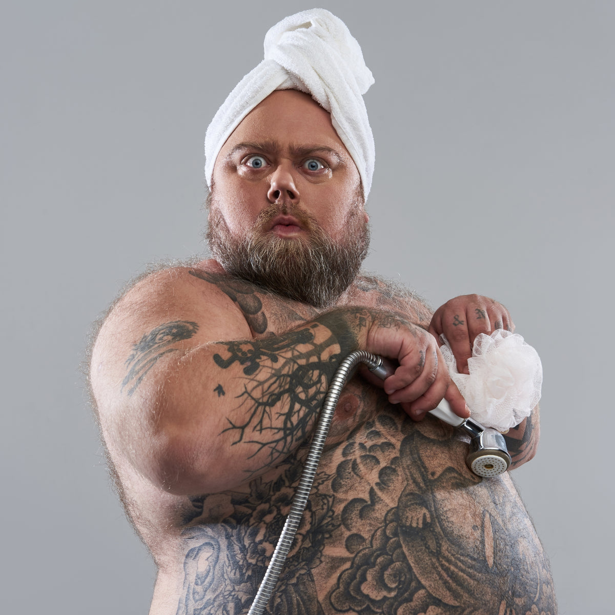 Heavyset tattooed man holding shower head.