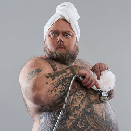 Heavyset tattooed man holding shower head.
