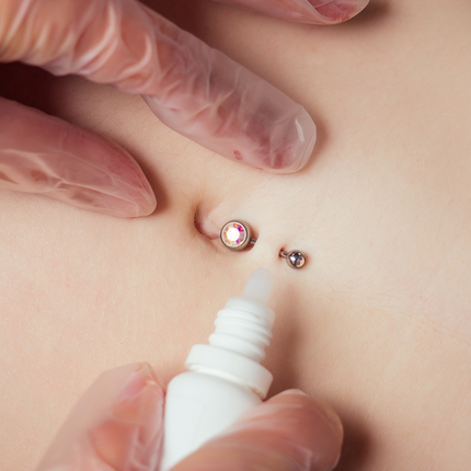 Person applying saline solution to a bellybutton piercing.