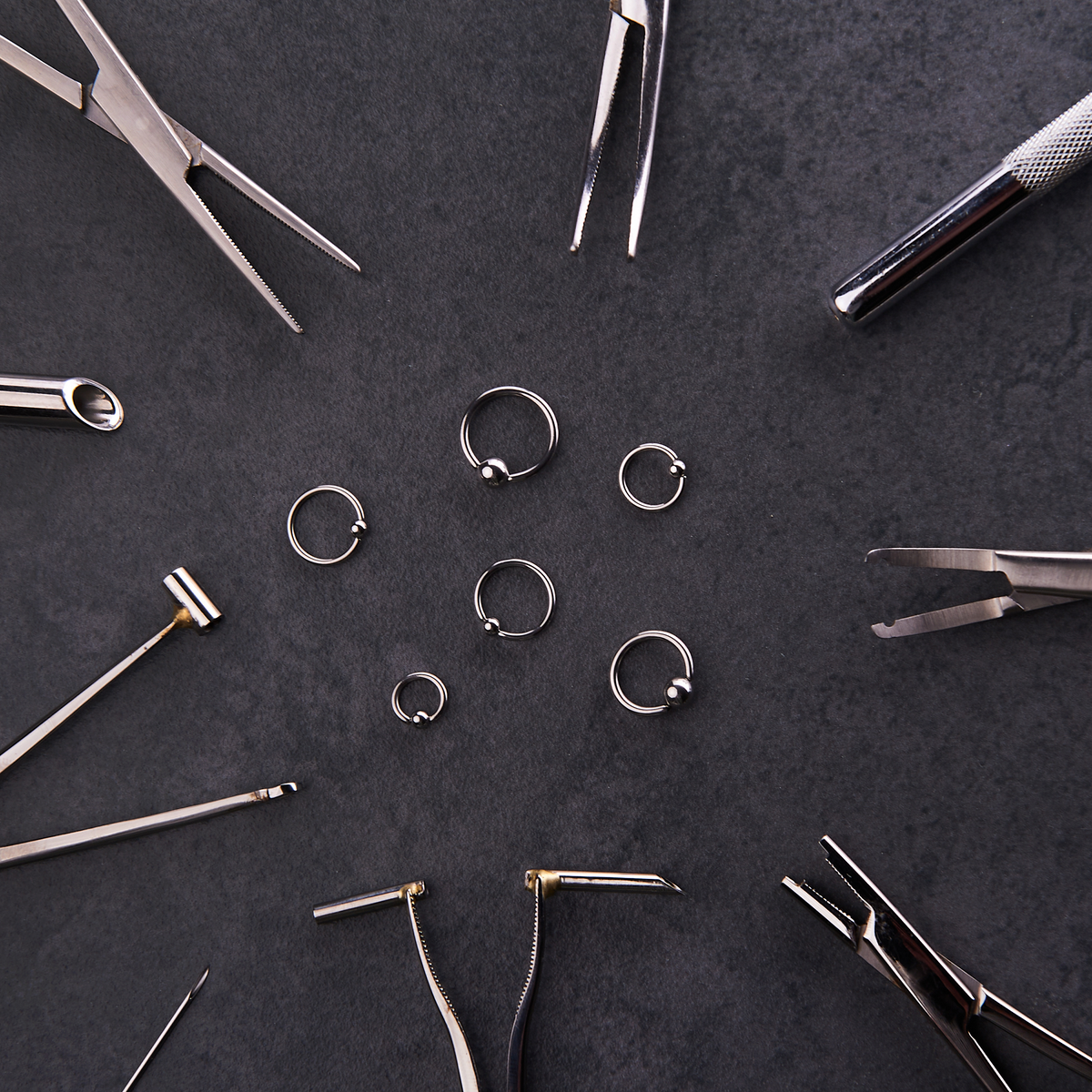 Circle of piercing tools and forceps around captive bead rings
