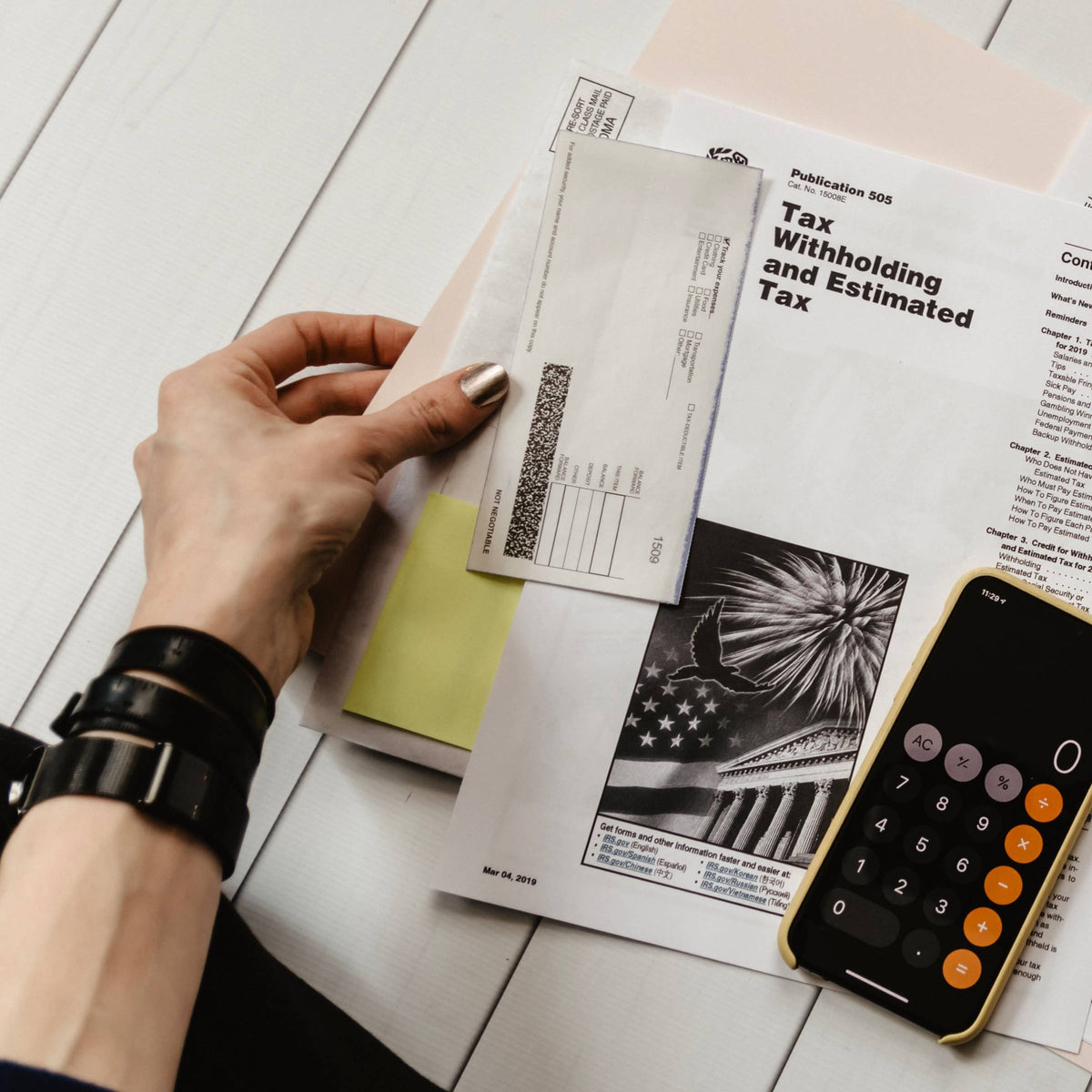 Hand with bracelets reviewing tax forms with a calculator