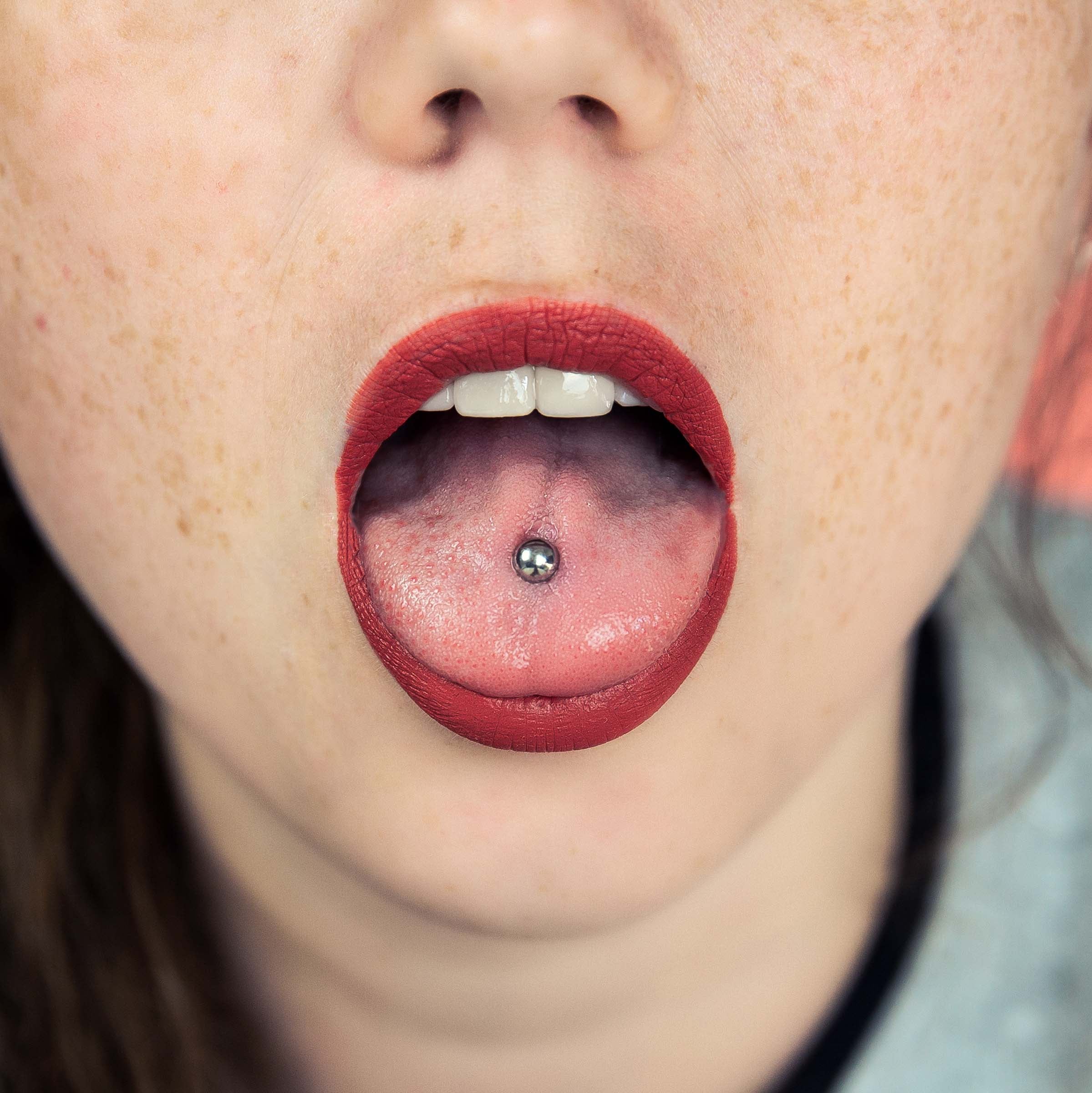 Close-up picture of client's tongue piercing with titanium body jewelry Worried You May Have an Infected Tongue Piercing? Signs, Symptoms, and Treatment