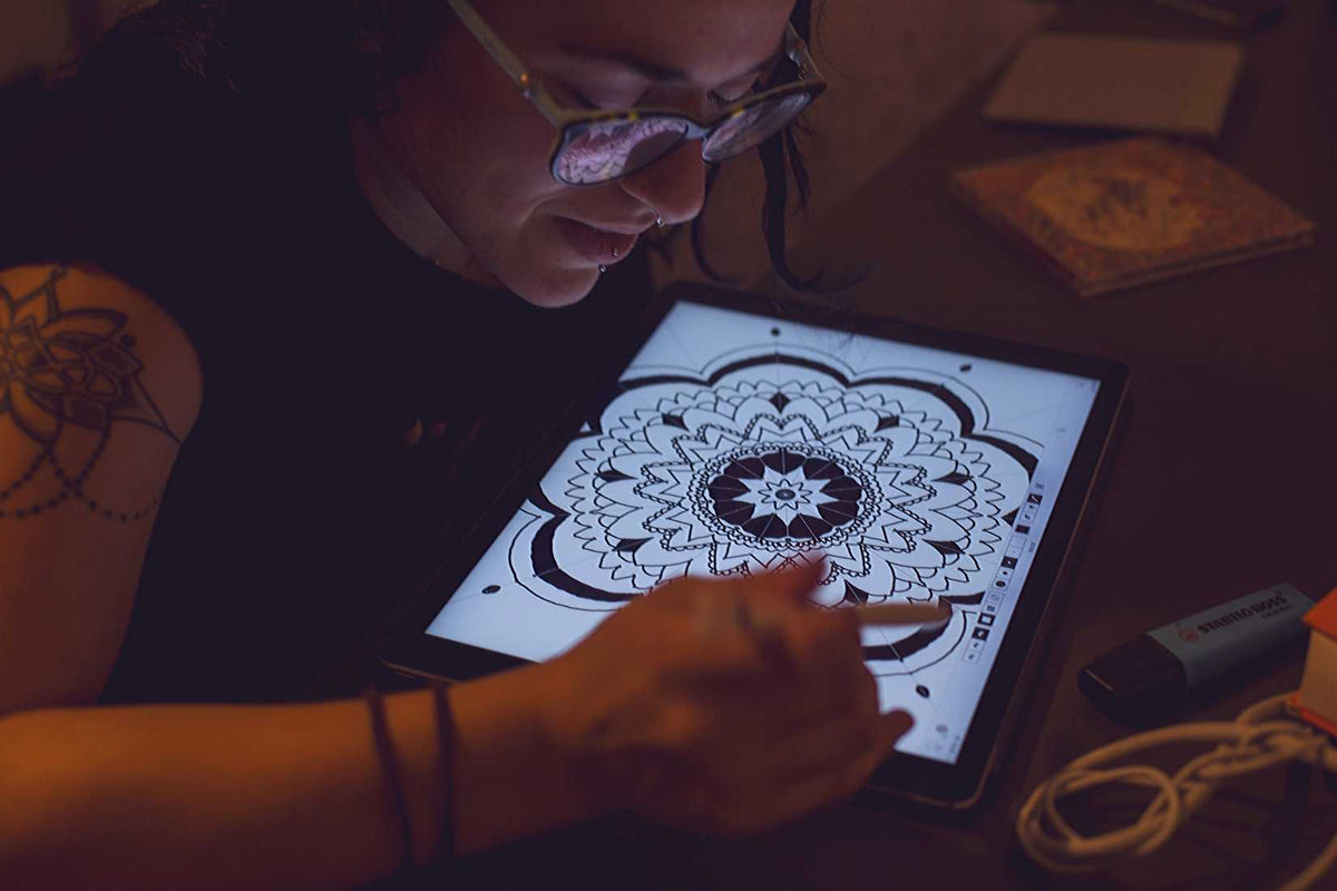 tattooed and pierced woman with glasses using a pen tablet to draw a mandala