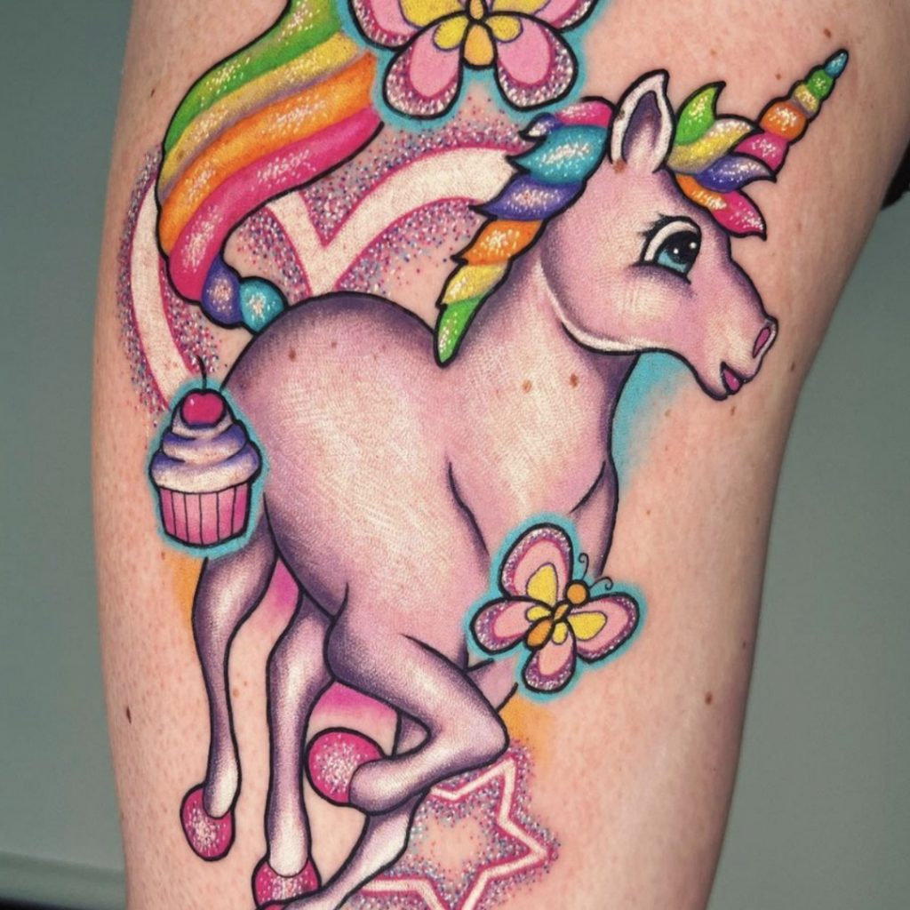 Tattoo of a Lisa Frank unicorn with a cupcake and butterflies by Amanda Graves
