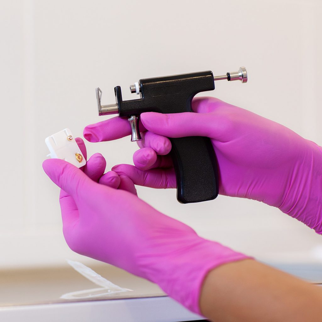 Close up image of piercing gun being used by piercer with pink latex gloves