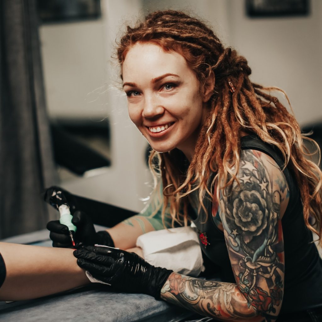 Tattoo artist working on a leg tattoo and smiling at the camera