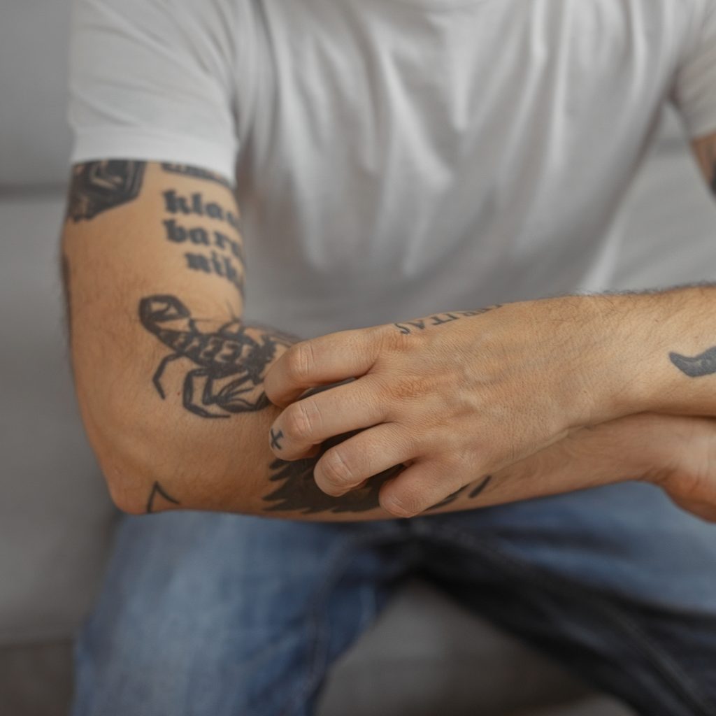 Man scratching his arm tattoo.