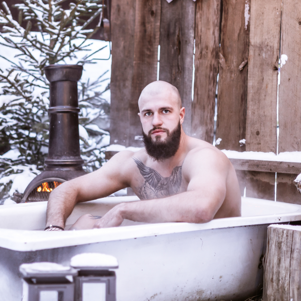 A tattooed man resting in a bathtub.